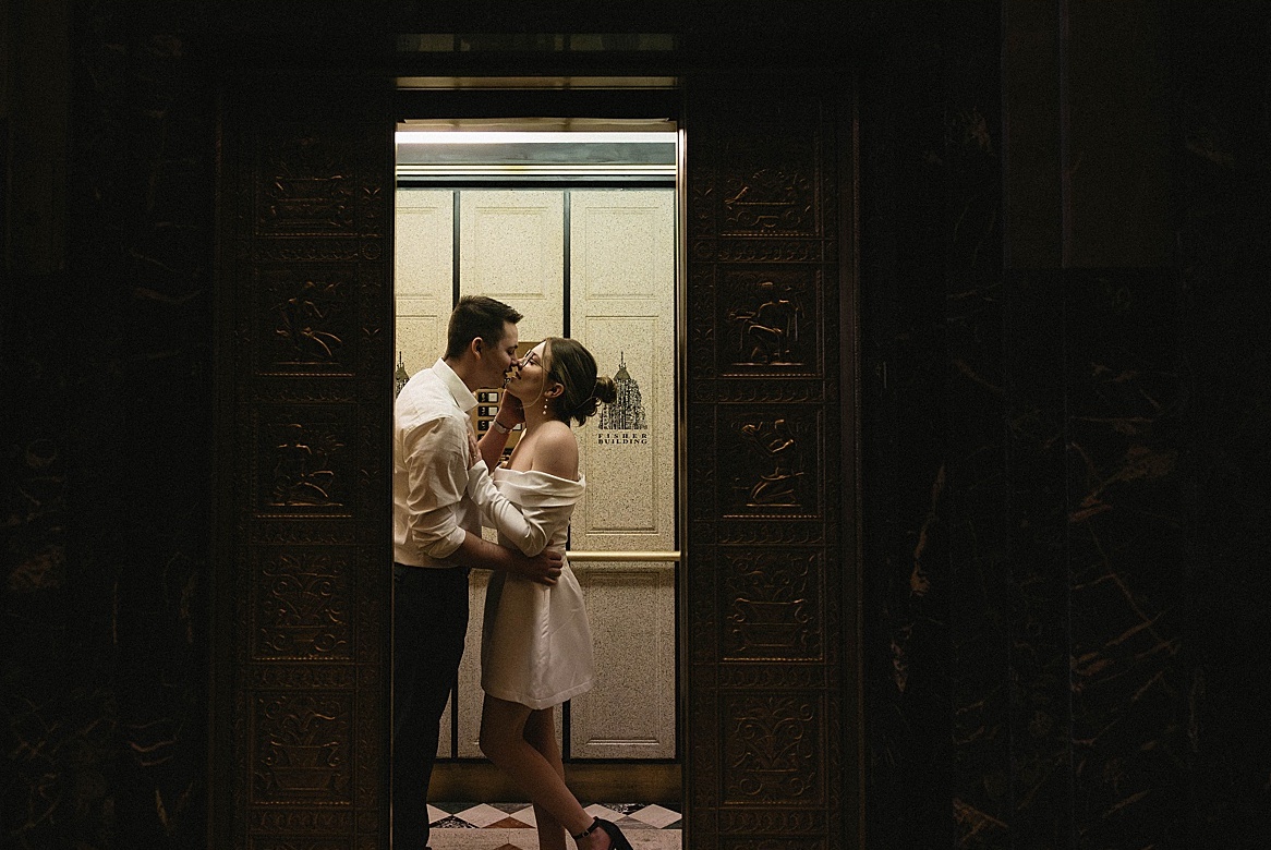 michigan couple's engagement photo - female in white dress and male in dress slacks and button down - standing close to each other, kissing in elevator