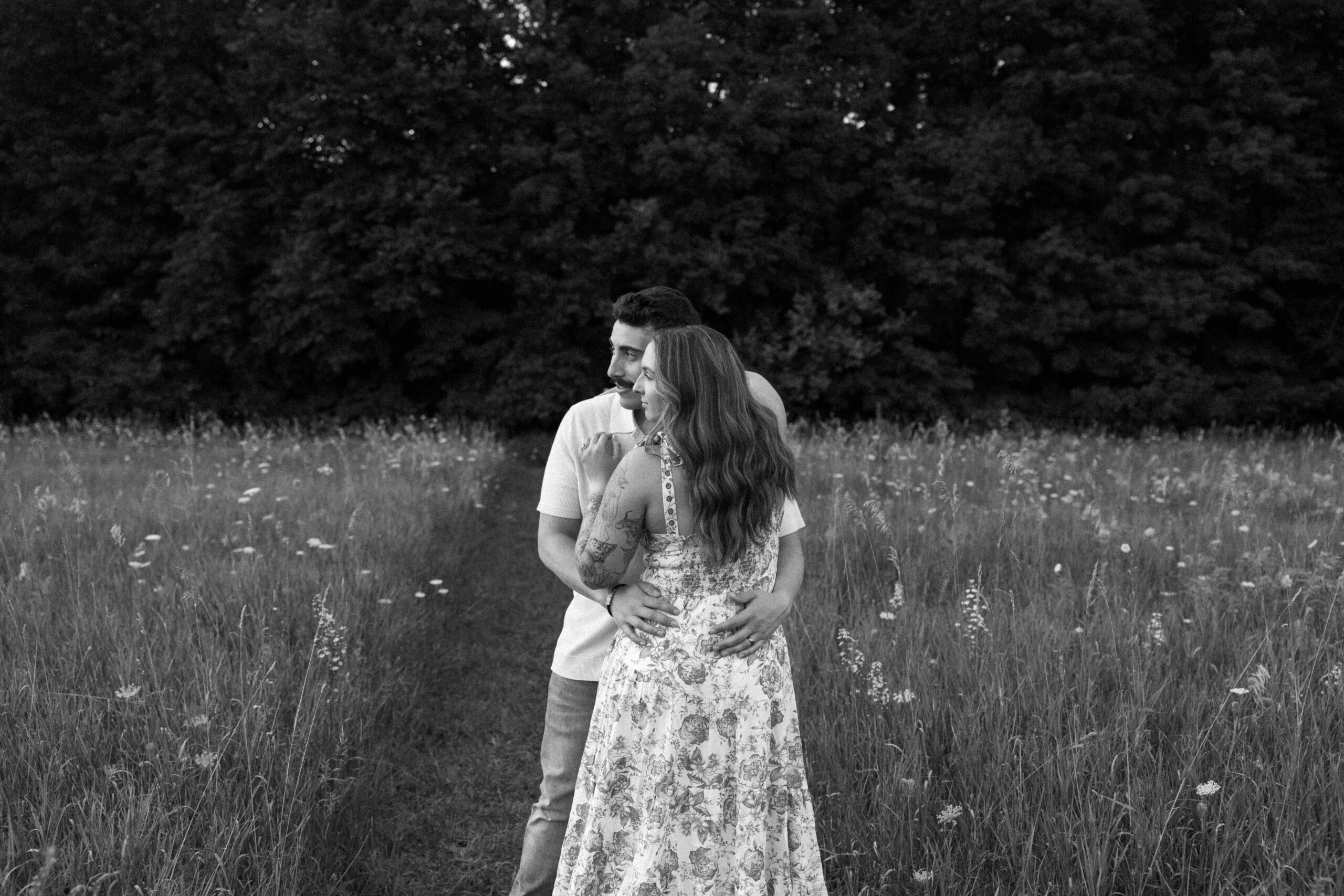 A couple embraces in a grassy field, surrounded by nature, showcasing love and connection in a serene setting.