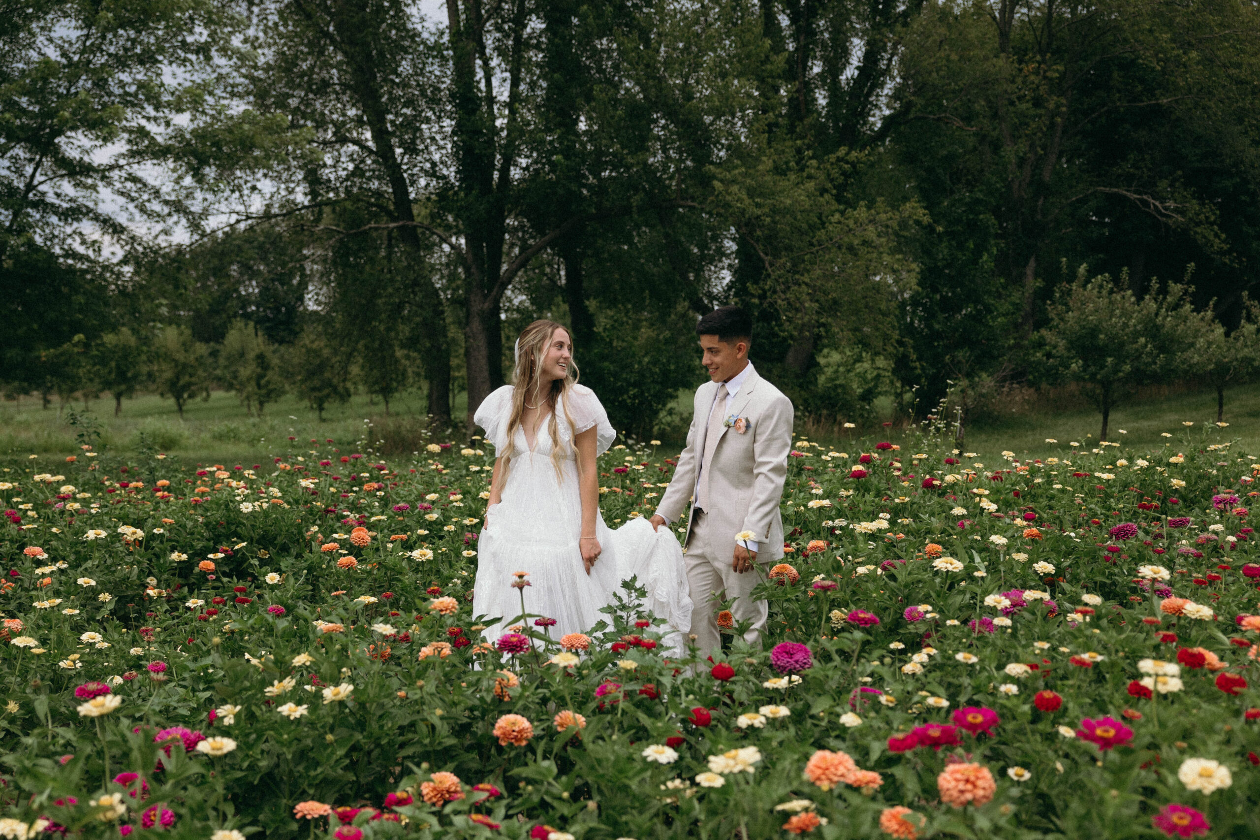 bride and groom on their wedding day in a field of bright flowers taking portraits together.