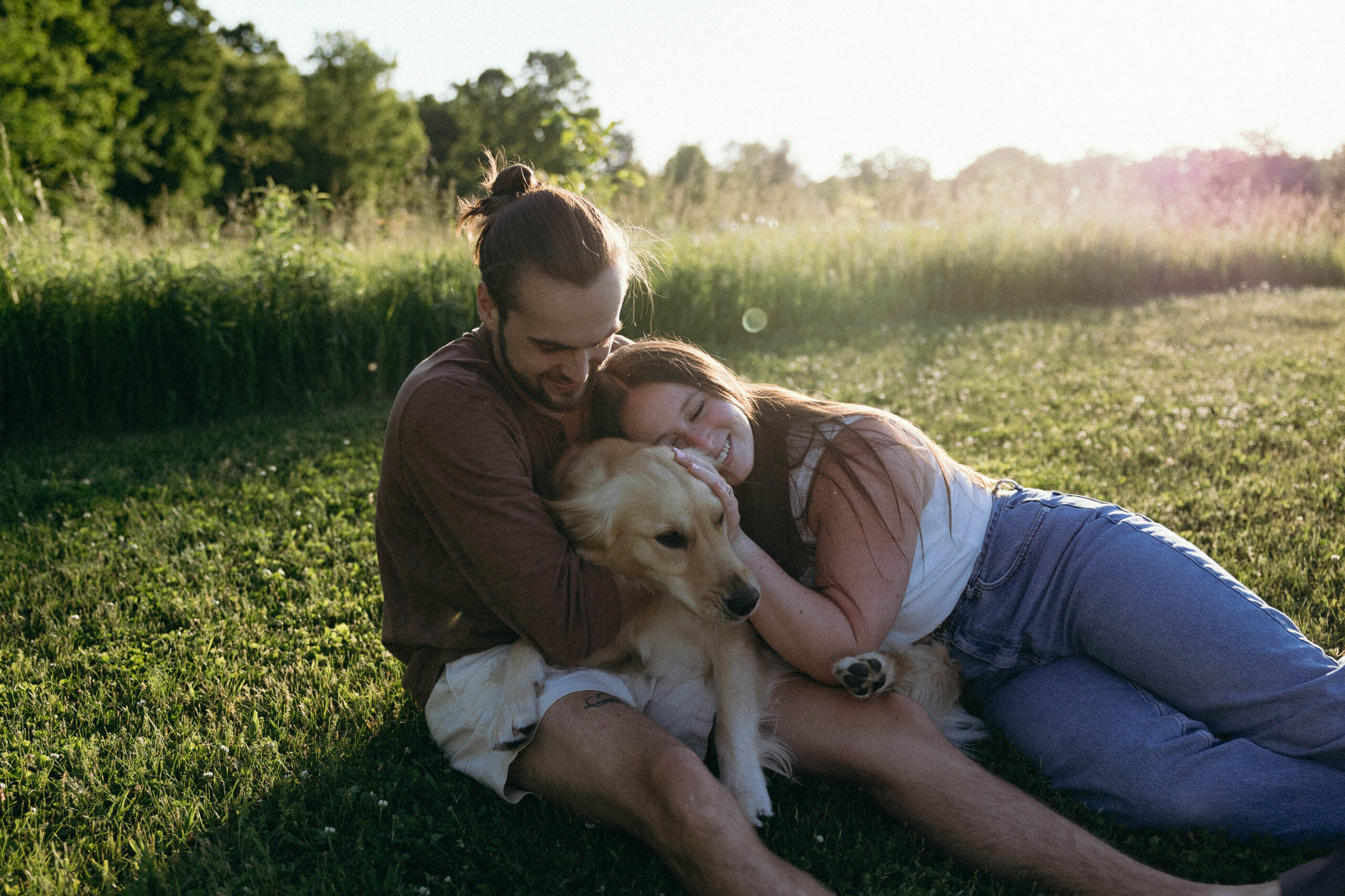 man and his wife cuddling their dog in a field at sunset.