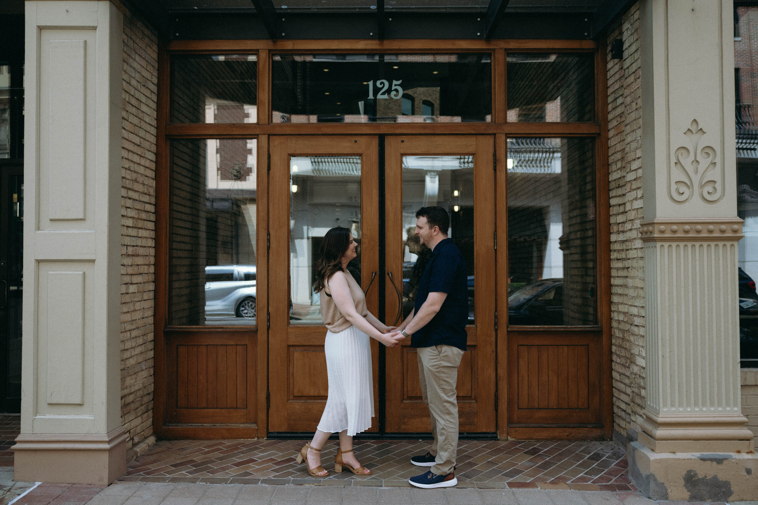Couple holding hands in front of a building's door, symbolizing unity and connection during their engagement photo session.