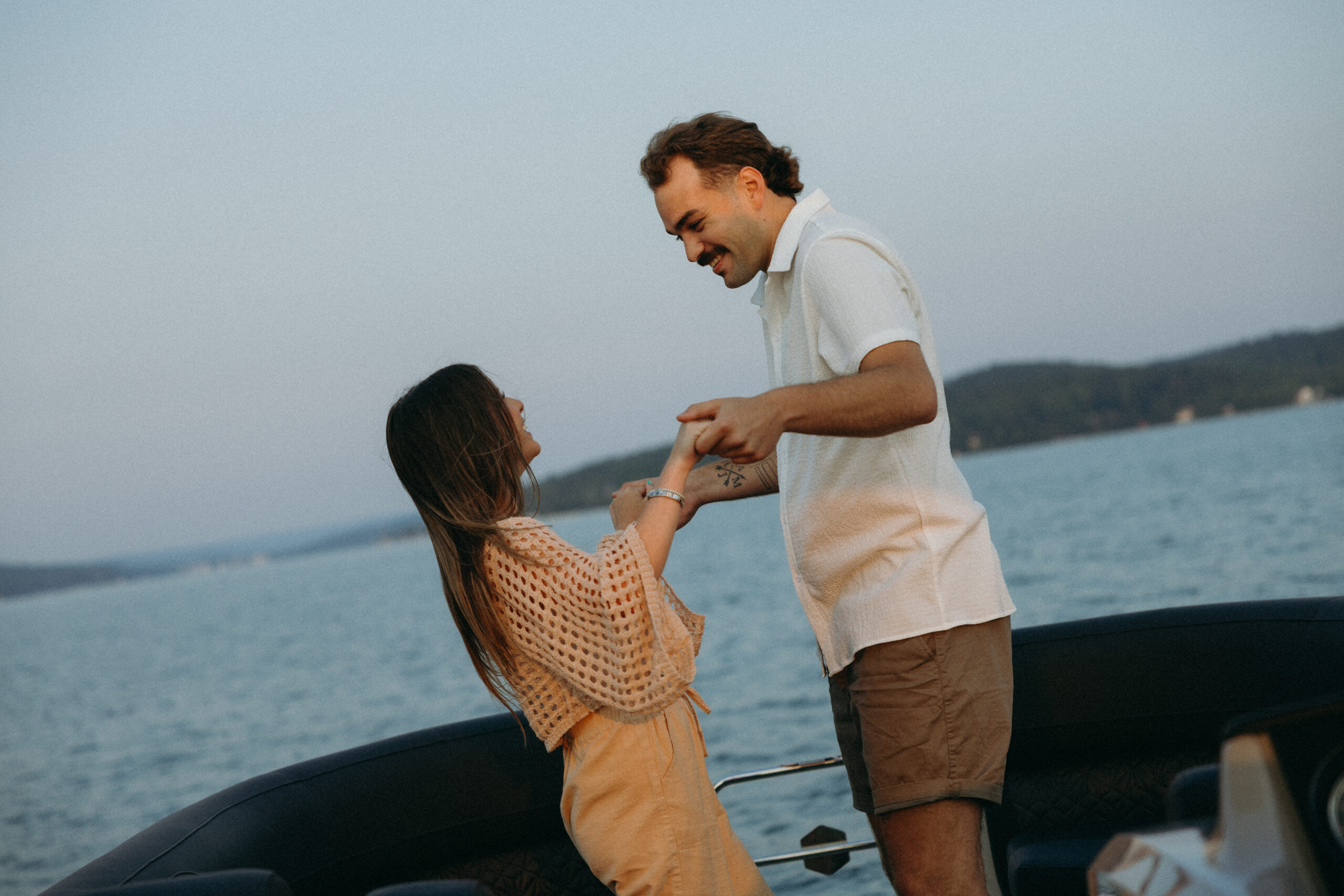 Woman and man dance near the front of a boat on a lake during sunset in Michigan.